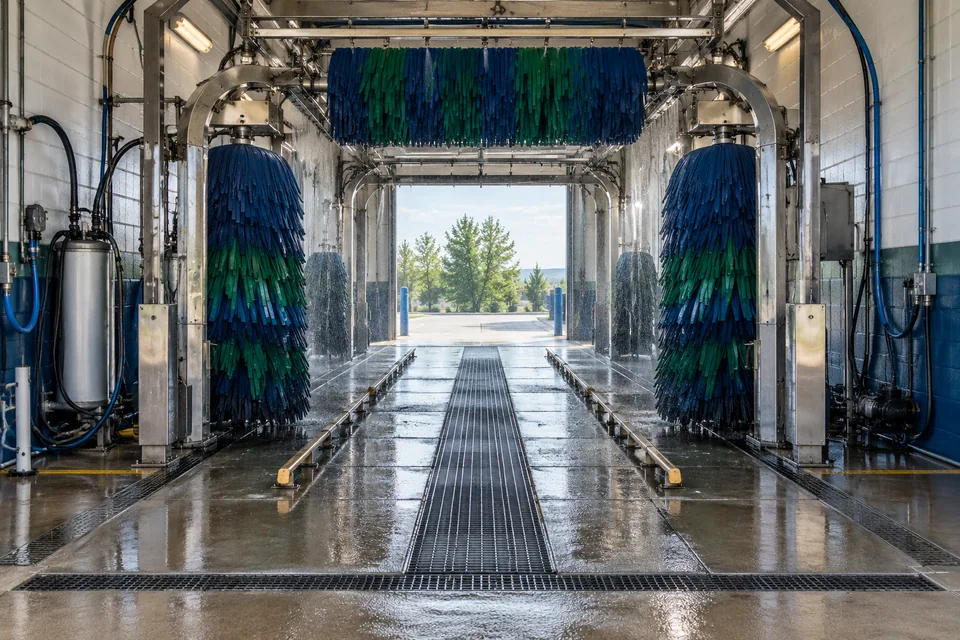 Illustrative automatic car-wash bay with brushes, spray equipment, and drainage.
